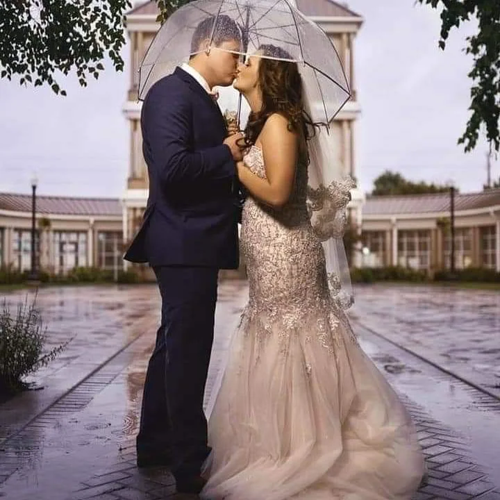 Bride and groom kissing beneath a clear umbrella at their wedding